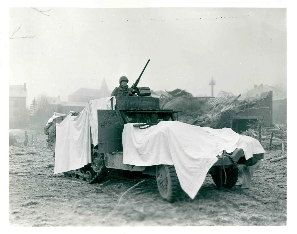 American half-track draped in white sheets near damaged buildings