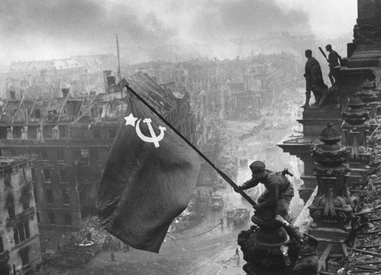 Yevgeny Khaldei’s photograph of a Soviet flag over the Reichstag, taken on 2 May 1945 after earlier flag raisings. This arranged and subsequently retouched image became a symbol of victory. Restoration by Adam Cuerden; public domain via Wikimedia Commons.