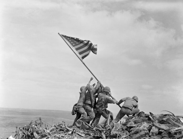 The second flag raising on Mount Suribachi, photographed by Joe Rosenthal on 23 February 1945. Public domain via Wikimedia Commons. The battle continued for weeks after this moment.
